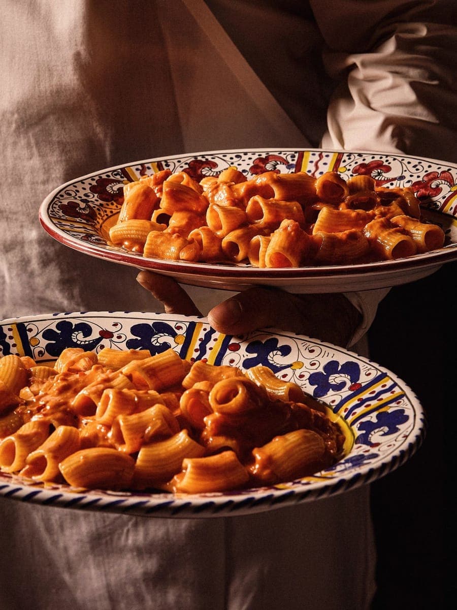 A waiter carrying two platters of spicy rigatoni on hand-painted plates at Carbone London