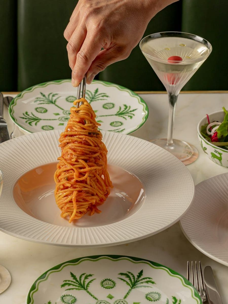 A marble table at Dante Mayfair set with pasta, a martini and green-bordered plates