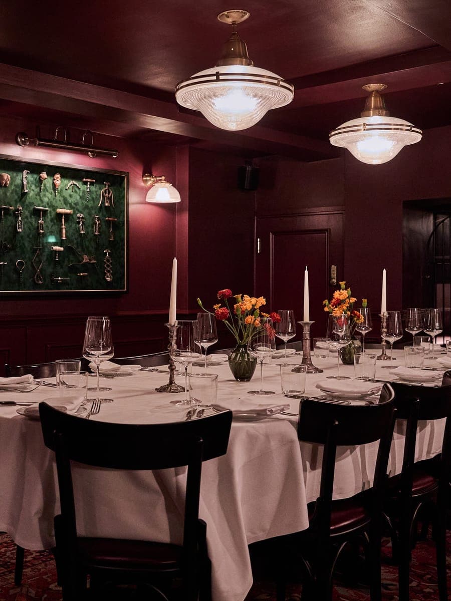 The maroon dining room at Noble Rot Mayfair, its wall hung with a framed corkscrew collection